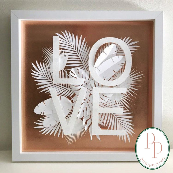Botanical paper cut collage with tropical foliage and clean, sans serif letters spelling LOVE on top of a metallic copper background. In white square shadowbox frame. 