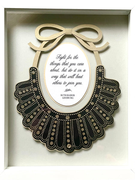 Papercut artwork of Ruth Bader Ginsburg's iconic Dissent Collar, framed in a white shadowbox. Quote inside reads, "Fight for the things that you care about, but do it in a way that will lead others to join you."